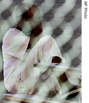 A detainee sits behind a chain-linked fence on the grounds of Camp Delta detention facility, at the Guantanamo Bay U.S. Naval Base, Cuba, Sep 2006)